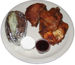 Baked chicken, baked potato and cranberry dinner plate.